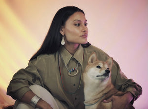 A model in holding a Shiba Inu while wearing muskox horn earrings and a necklace with beaded details with a silver cuff.