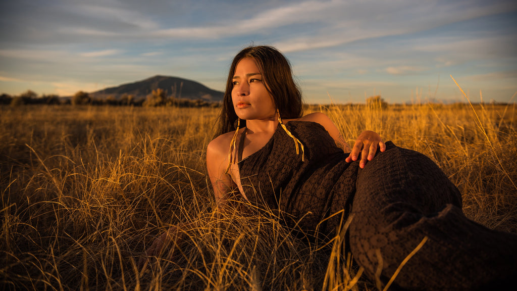 Morningstar lays in a grass field modelling some caribou hide earrings. 